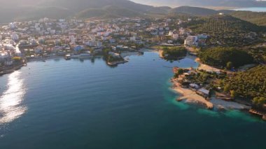 Ksamil şehrinin insansız hava aracı görüntüsü, yoğun bir otel ve ev kümesi, ve yüzen platformları ve plaj kulüpleri olan ikonik parlak mavi koylar.