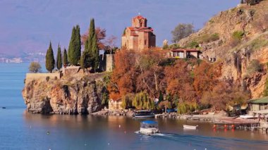 Kaneo 'daki St. John Kilisesi' nin hava aracı görüntüsü kayalık uçurumlar, sonbahar ağaçları ve kıyı şeridi boyunca kenetlenmiş küçük botlarla çevrili.