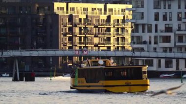 Kopenhag, Danimarka - 6 Ağustos 2025: Yolcuları modern şehir manzarası binalarının yanındaki bir kanal boyunca taşıyan sarı su otobüsü