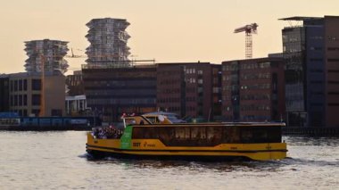 Kopenhag, Danimarka - 6 Ağustos 2025: Sarı liman otobüsü arka planda şehir binaları olan turistleri denize taşıyor