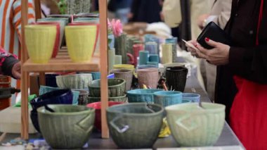 El yapımı çömlek parçaları açık hava pazarındaki bir tezgahta gezinen bir kişi tarafından görüntülenir.
