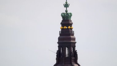 Bulutlu gökyüzünün altında birden fazla süslü taç bulunan Christiansborg Sarayı kulesi.