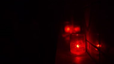 Cam kavanozdaki kırmızı mum, yakınlardaki bir yüzeye yansıyan sıcak bir parıltı saçıyor. Karanlık kulüp atmosferi