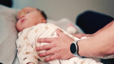 Bebek yastıklı bir yüzeyde yatarken yetişkin eller nazikçe bebeğin gövdesine yaslanır.