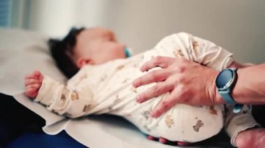 Bebek yastıklı muayene masasında yatarken, bakıcılar rutin bir kontrol sırasında vücudu nazikçe desteklerler.