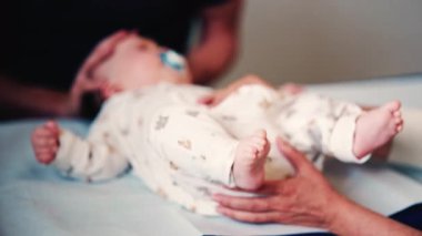 Bebek yastıklı muayene masasında yatarken, bakıcılar rutin bir kontrol sırasında vücudu nazikçe desteklerler.