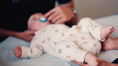 Bir yetişkinin bebeğin elini nazikçe tutarken diğer bir bakıcı da sağlık kontrolü sırasında bebeğin başını desteklerken.