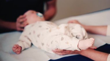 Bir yetişkinin bebeğin elini nazikçe tutarken diğer bir bakıcı da sağlık kontrolü sırasında bebeğin başını desteklerken.