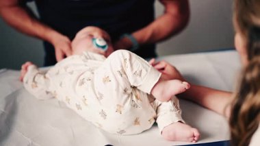 Bir bebeğin bacaklarını ve ayaklarını kapatırken, bakıcı bakımı sırasında ya da muayene sırasında bebeği nazikçe yeniden konumlandırır.