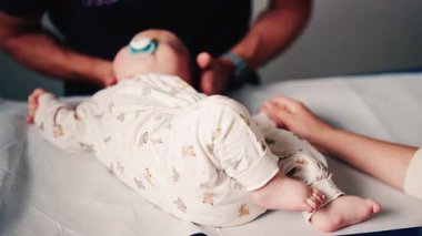 Bir bebeğin bacaklarını ve ayaklarını kapatırken, bakıcı bakımı sırasında ya da muayene sırasında bebeği nazikçe yeniden konumlandırır.