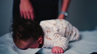 Bebek, yastıklı bir yüzey üzerinde karnını çalıştırırken bebek bakıcısı nazikçe bebeğin sırtını destekliyor.