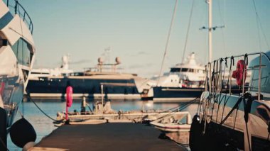 Gün ışığında her iki tarafında da demirlemiş yatları olan bir marina rıhtımının manzarası