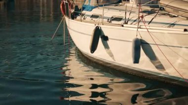 Yelkenli mavi gölgelikli ve sakin su yansımalı bir marinaya yanaştı.