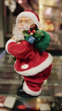 Noel Baba heykelciği küçük hediyelerle süslenmiş yeşil bir hediye çantası tutuyor, hareket ediyor. Dikey