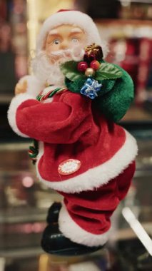 Noel Baba heykelciği küçük hediyelerle süslenmiş yeşil bir hediye çantası tutuyor, hareket ediyor. Dikey