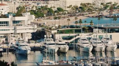 Mavi bir Akdeniz kıyısı boyunca yanaşmış yatları olan lüks bir yat limanının geniş açılı görüntüsü.