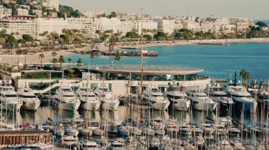 Mavi bir Akdeniz kıyısı boyunca yanaşmış yatları olan lüks bir yat limanının geniş açılı görüntüsü.