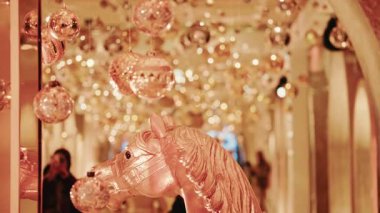 Altın tatil ışıkları ve süslemelerle dolu sıcak ışıklı bir koridorda sergilenen dekoratif bir at heykelinin zarif yakın çekimi.