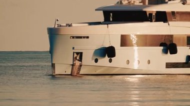 Uzaktaki deniz feneriyle sakin deniz suyunda hareket eden modern lüks bir yatın yan görüntüsü.