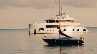 Fransız Rivierası yakınlarındaki sakin Akdeniz sularına demirlemiş lüks bir karavan ve ön planda daha küçük bir yelkenli.