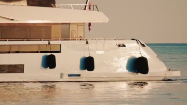 Uzaktaki deniz feneriyle sakin deniz suyunda hareket eden modern lüks bir yatın yan görüntüsü.