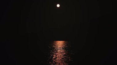 Minimalist gece sahnesi Ay 'ın sakin deniz suyuna yansıdığını gösteriyor