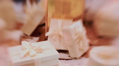 Karlı dekoratif bir yüzeye yerleştirilmiş beyaz, kurdeleli hediye kutularını kapatın. Arka planda sıcak ortam aydınlatması ve şenlikli aksesuarlar olsun.