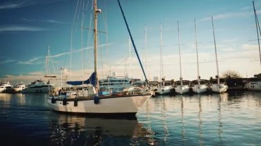 Cannes, Fransa - 22 Aralık 2025: Bir marina havzasında dinlenen beyaz bir yelkenli, açık mavi gökyüzünün altında demirlemiş yatlar ve uzun direklerle çevrili.