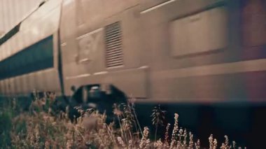 Arka planda endüstriyel dokular ve şehir unsurları ile kentsel bir ortamda demiryolu boyunca hareket eden bir yolcu treninin yan görüntüsü