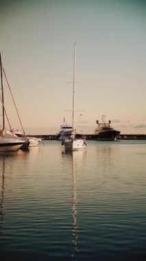 Yelkenli ve direklerin soyut bileşimi günbatımında durgun suya yansıyarak simetrik ve sakin desenler oluşturur. Dikey