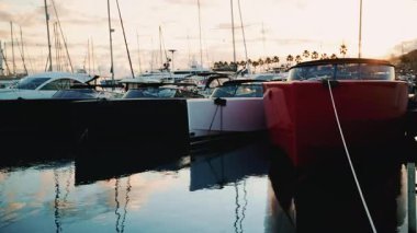 Kırmızı ve beyaz motorlu tekneleri bir rıhtımda yan yana demirlemiş, altın gün batımı ışığı suya yansıyor.