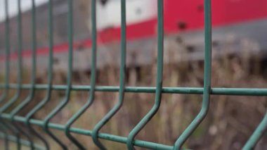 Yolcu treni geçiyor, yukarıdaki elektrik kabloları ve etrafındaki binalarla çerçevelenmiş.