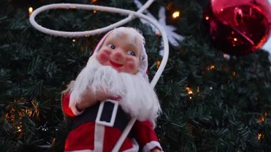 Noel Baba dekorasyonu, Noel ağacı dalları ve sıcak tatil ışıklarıyla çerçevelenmiş açık havada sergilendi.