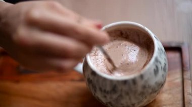 Seramik bardakta sıcak çikolata karıştırmak kremalı köpük yaratıyor.