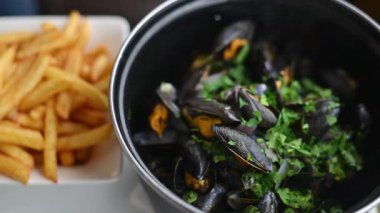 Pişirilmiş midye, yanında altın patates kızartması ve otlarla birlikte bir tencerede servis edilir.