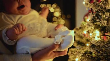 Süslü bir Noel ağacına yakın tutulan bebek, aydınlatılmış süs ve ışıklara doğru uzanıyor.