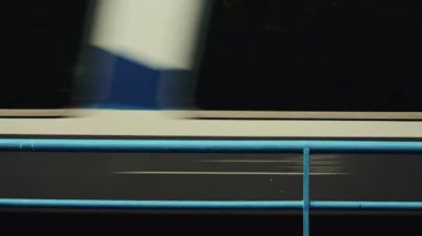 Demiryolu kenarındaki mavi bir çitten geçen bir yolcu treninin yan görüntüsü.