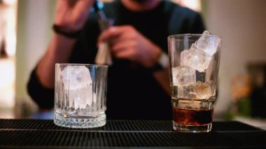 Bir barmen metal bir jigger 'dan temiz buz küpleriyle dolu uzun bir bardağa ruh döker.