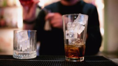 Bir barmen metal bir jigger 'dan temiz buz küpleriyle dolu uzun bir bardağa ruh döker.
