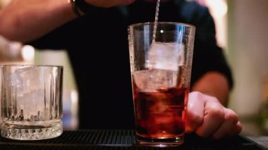 Barmenin bardağında uzun bir kaşık ile kırmızı kokteyl karıştırırken yakın plan.