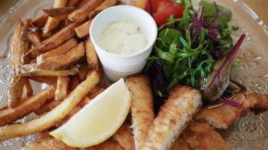 Kızarmış patates, taze salata, limon dilimi ve kremalı sos ile servis edilen balık ve patates kızartması.