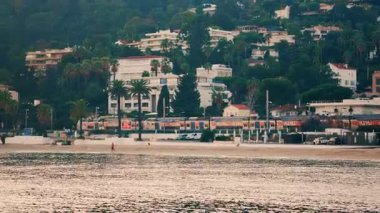 Golfe Juan, Fransa - 22 Aralık 2025: Sahil şeridine paralel giden kıyı trenleri, arka planda palmiye ağaçları, sahil kıyısı ve yamaçtaki konut binaları