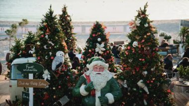 Cannes, Fransa - 23 Aralık 2025: Noel Baba heykeli deniz kenarındaki bir tatil pazarında süslü Noel ağaçlarının arasına yerleştirildi