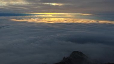 Panoramik hava aracı bulutların üzerindeki altın güneş doğuşunu, dağlardaki kış manzarasını görüyor. Romanya 'da Transilvanya ve Ciucas Dağı