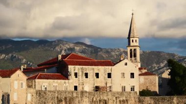 Budva Eski Kasabası tarihi mimariyi, kırmızı çatıları ve dağlara karşı Sveti Ivan Kilisesi çan kulesini gösteriyor.