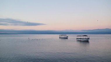 Huzurlu bir gündoğumunda ya da günbatımında iki küçük tekne dingin suyun üzerinde dinleniyor. Ohri Gölü, Kuzey Makedonya