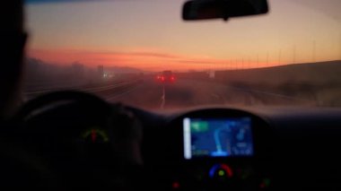 Arabanın iç perspektifi gün doğumunda yoğun siste otoyola çıkıyor.