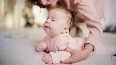 Bebek yumuşak bir yüzeyde karın çalışması yaparken, ebeveyn arkadan destek veriyor.