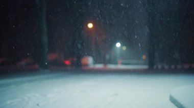 Geceleri sürekli olarak boş bir parka kar yağıyor. Kar zemini kaplarken sokak lambaları arka planda hafifçe parlıyor.