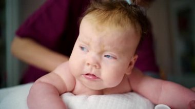 Baby resting comfortably on a soft cushion while a caregiver remains close for support
